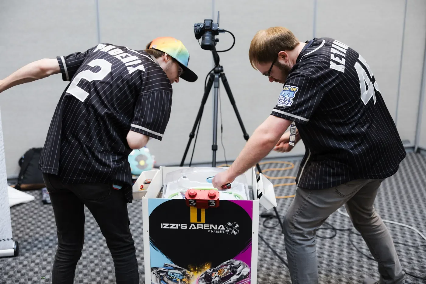 Two adults playing at a tabletop arena branded Izzi's Arena