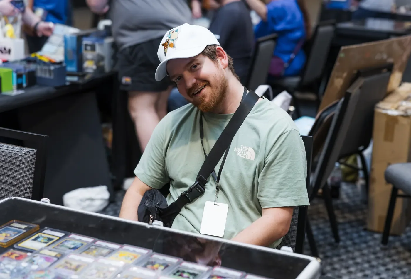 A smiling card vendor seated behind a glass display case at IZZISCON