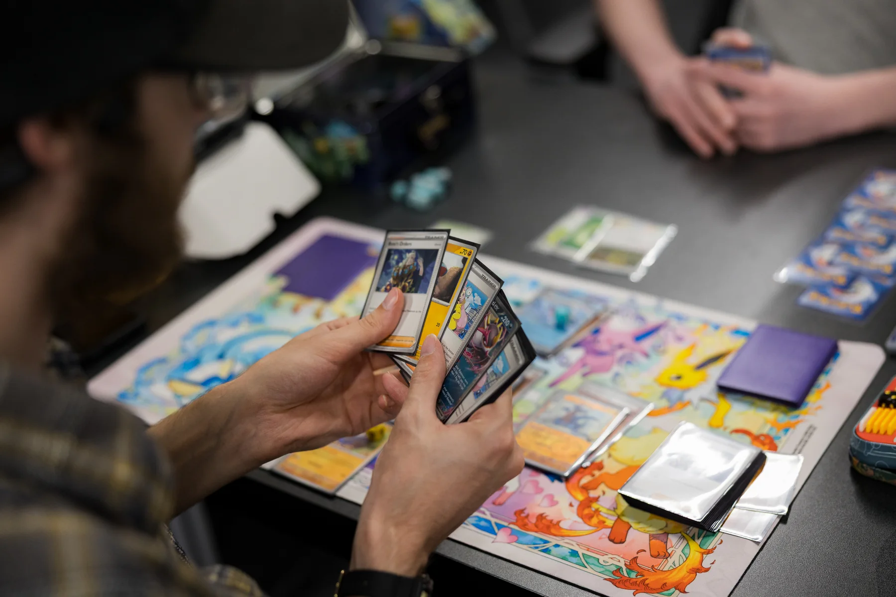 A player holds Pokémon cards over a colorful playmat at Izzi's Gym