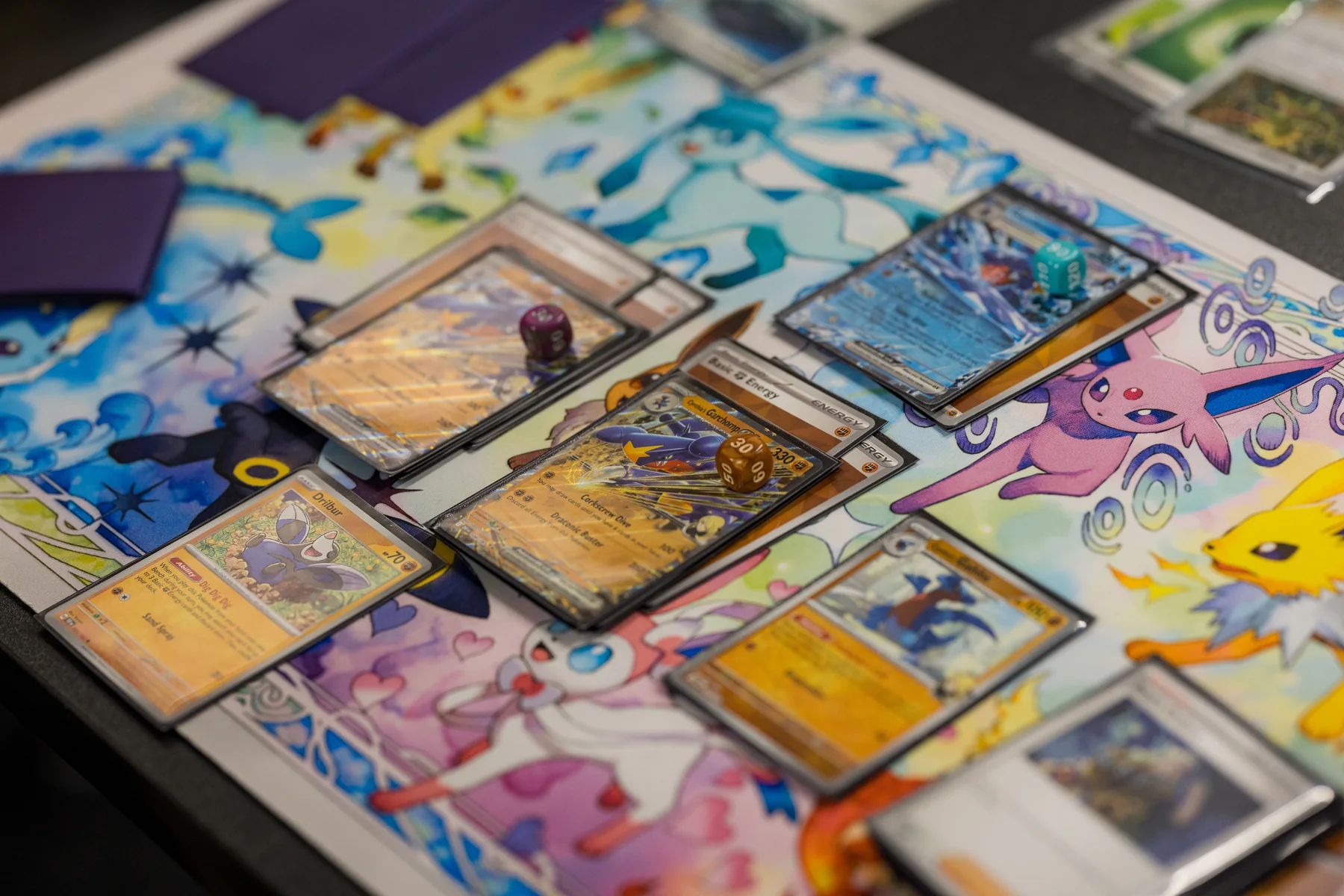 Pokémon cards, dice, and sleeves spread across a colorful playmat at Izzi's Gym